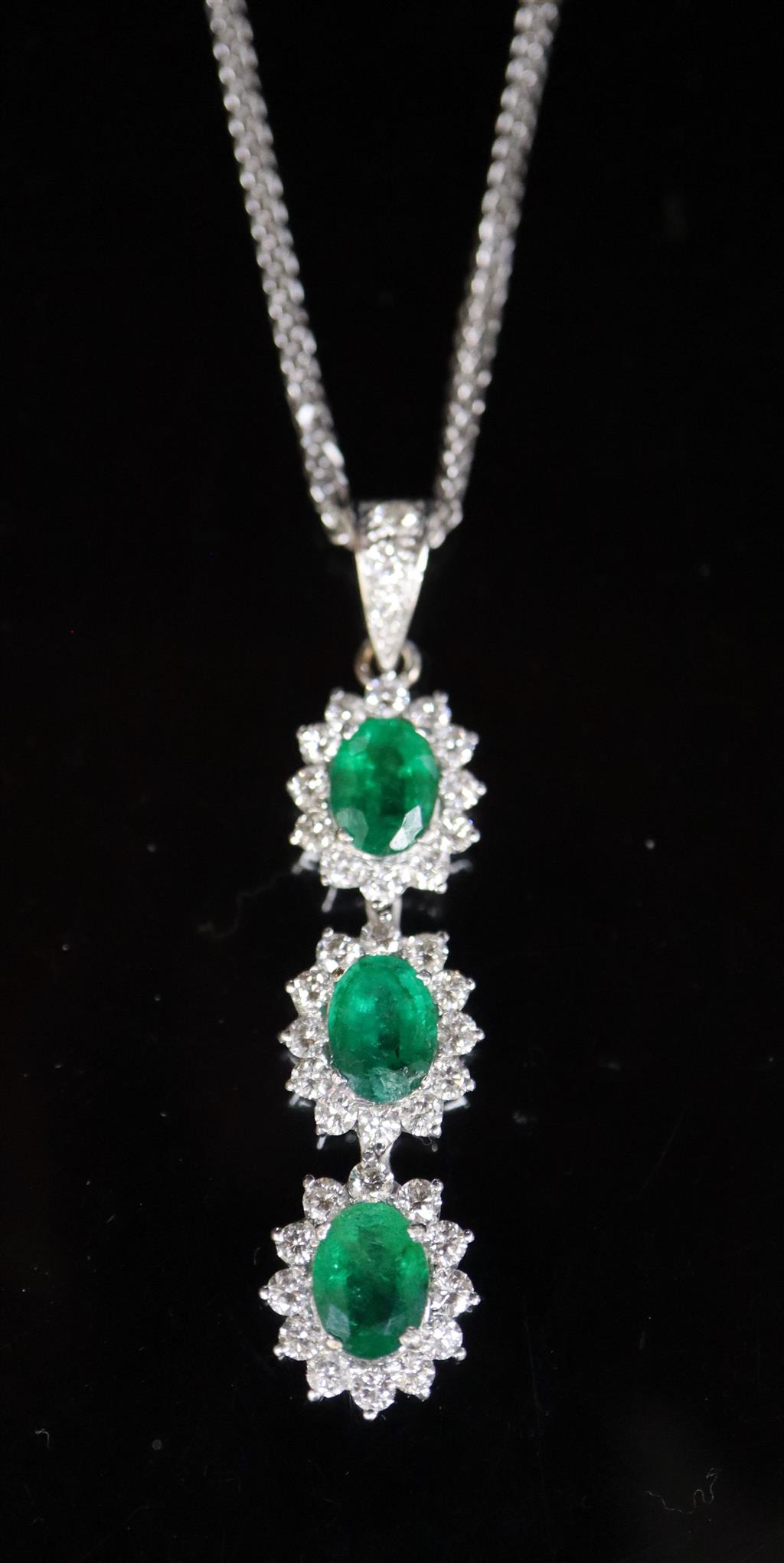 A modern 18ct white gold, emerald and diamond set oval triple cluster drop pendant, on an 18ct white gold chain,